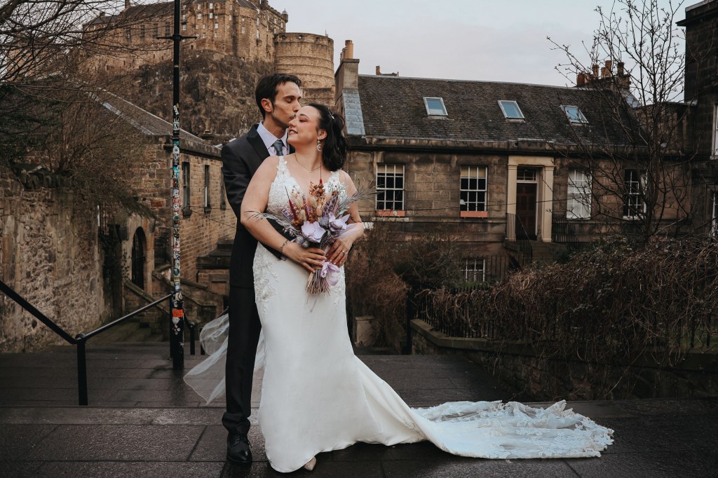 Bride and groom participating in an elopement / wedding photoshoot at The Vennel steps in front of Edinburgh Castle.